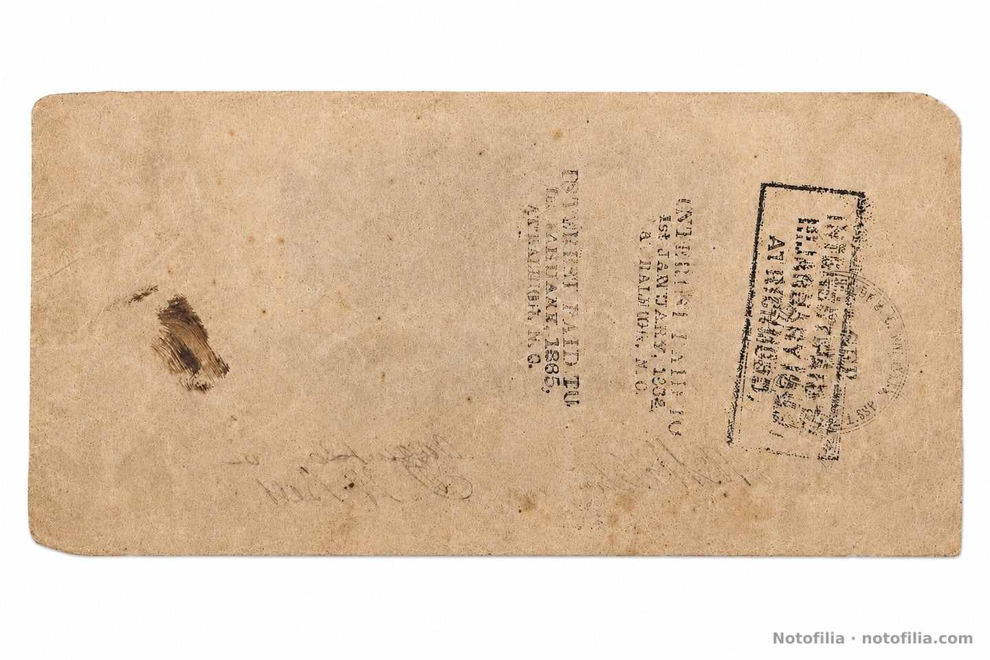 Reverso sin diseño impreso, con sellos de pago de interés: «INTEREST PAID TO 1st JANUARY, 1864» y «…1865, AT RALEIGH, N.C.», y un tercer sello en recuadro parcialmente ilegible.