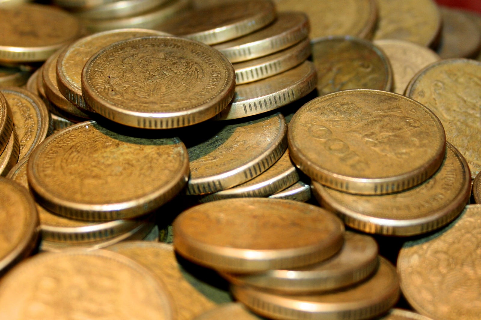 Montón de monedas mexicanas de peso en circulación, con el escudo nacional y cantos estriados