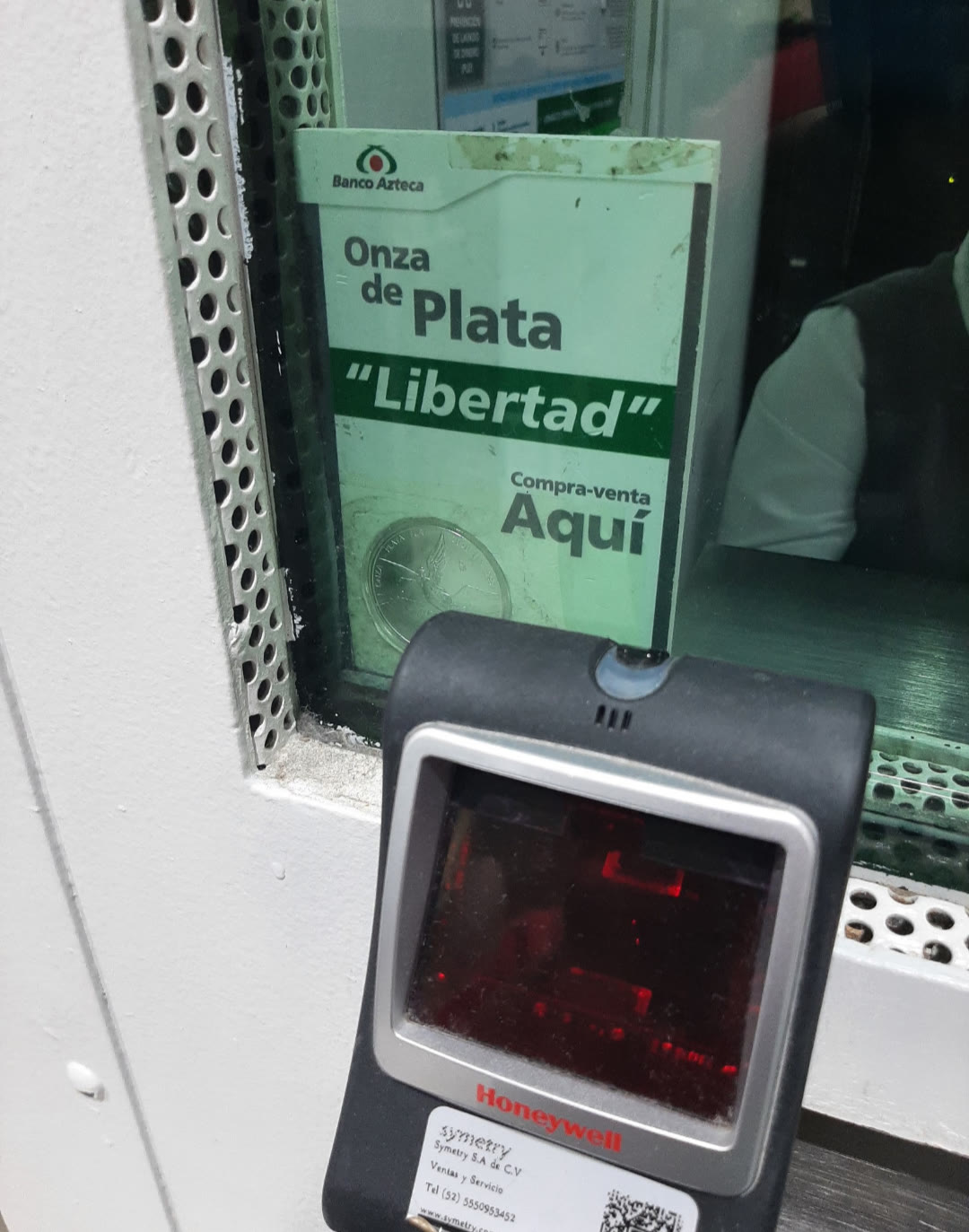Letrero de Banco Azteca en una ventanilla: Onza de Plata Libertad, compra-venta aquí, con un escáner en primer plano