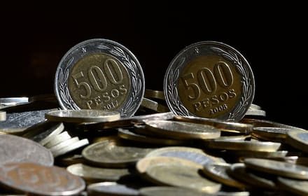 Two Chilean bimetallic 500-peso coins on their edge over a pile of coins, with the years visible on the reverse