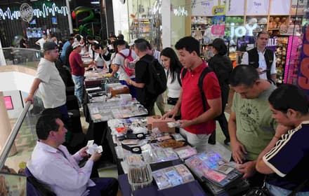 Visitors and exhibitors review note albums and collector pieces at tables of a numismatic meeting